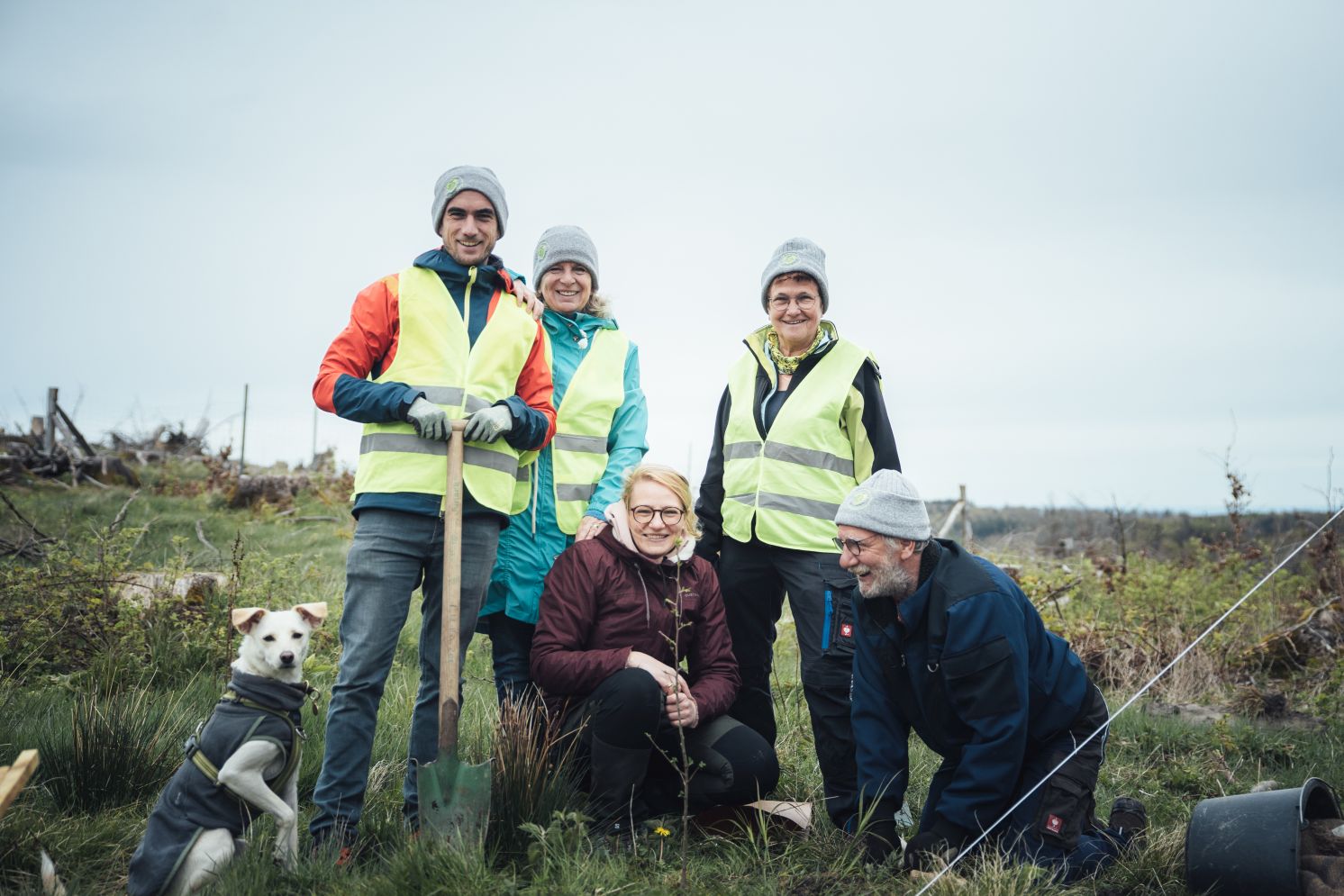 Eine Gruppe von Freiwilligen mit Hund posiert lachend nach einer Pflanzaktion im Herzenswald